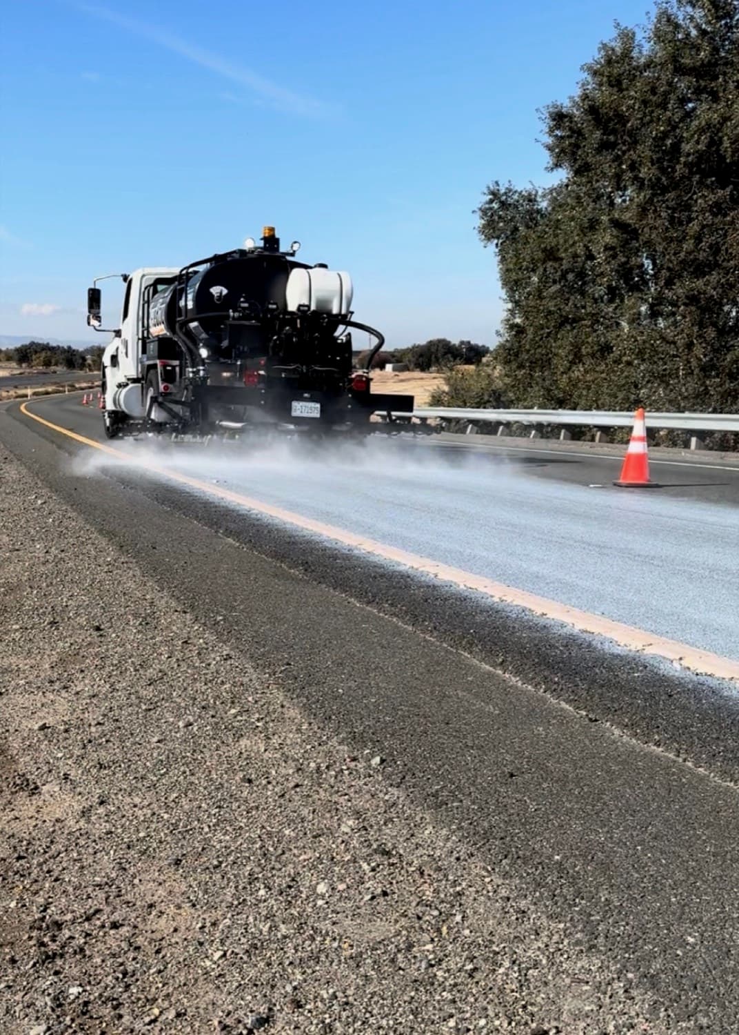 Distributor truck spraying pavement beside traffic cones in daylight