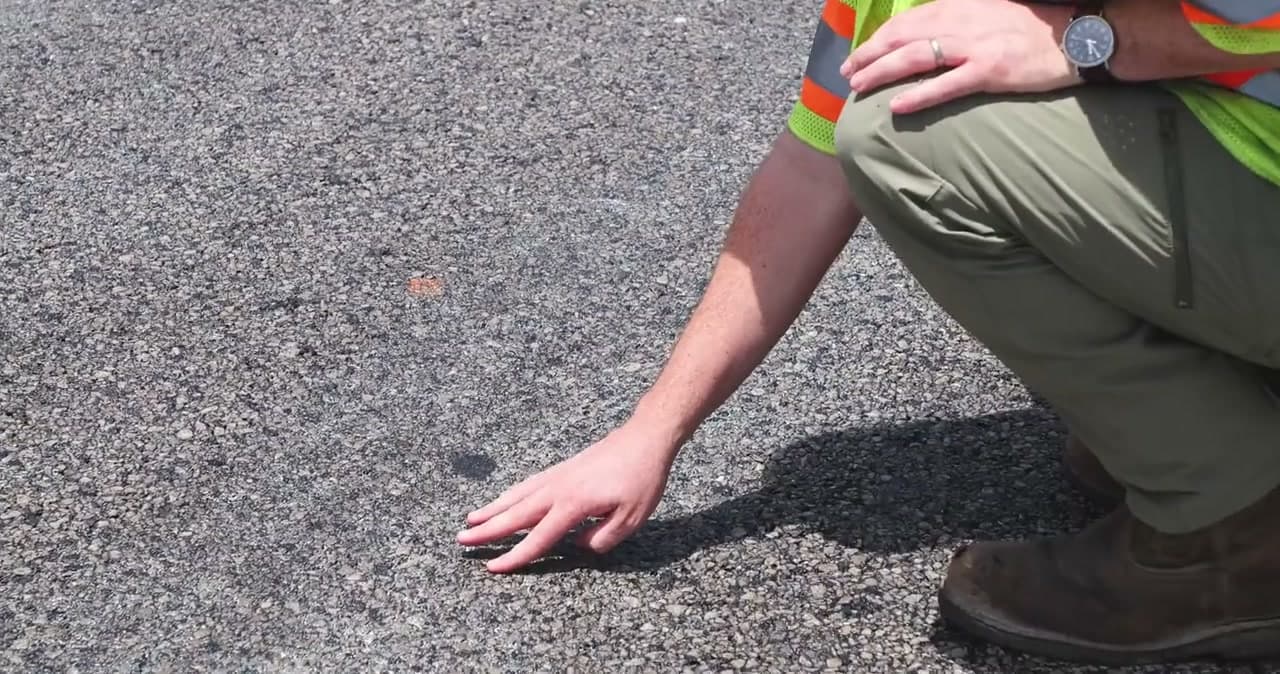 A hand pressed onto a freshly treated pavement surface beside a kneeling crew member's boot
